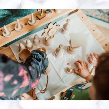 Child playing with natural wood Montessori-style religious figures and wooden pieces on a white mat.
